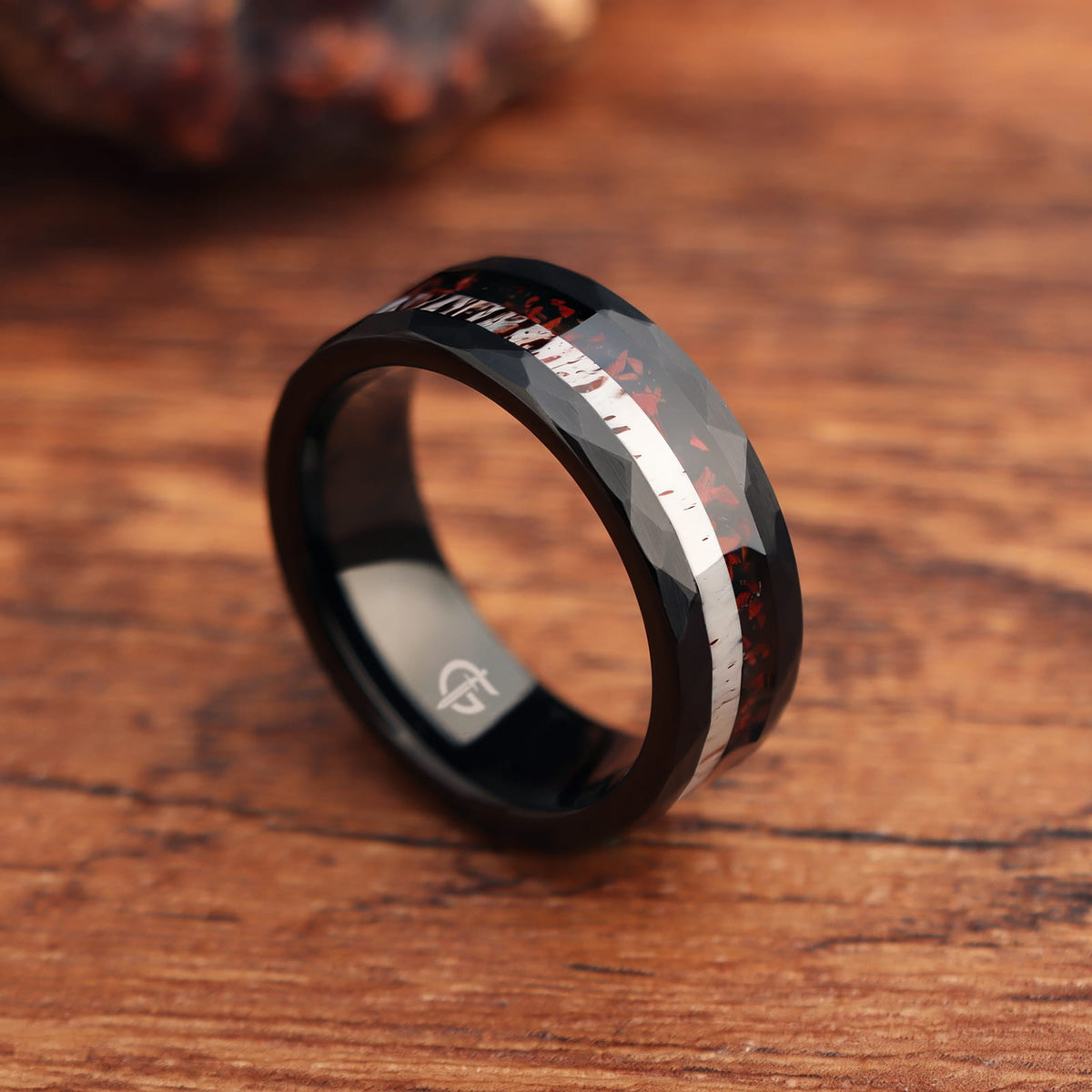 Hammered black tungsten ring with red dinosaur bone beside pale deer antler in a single center inlay