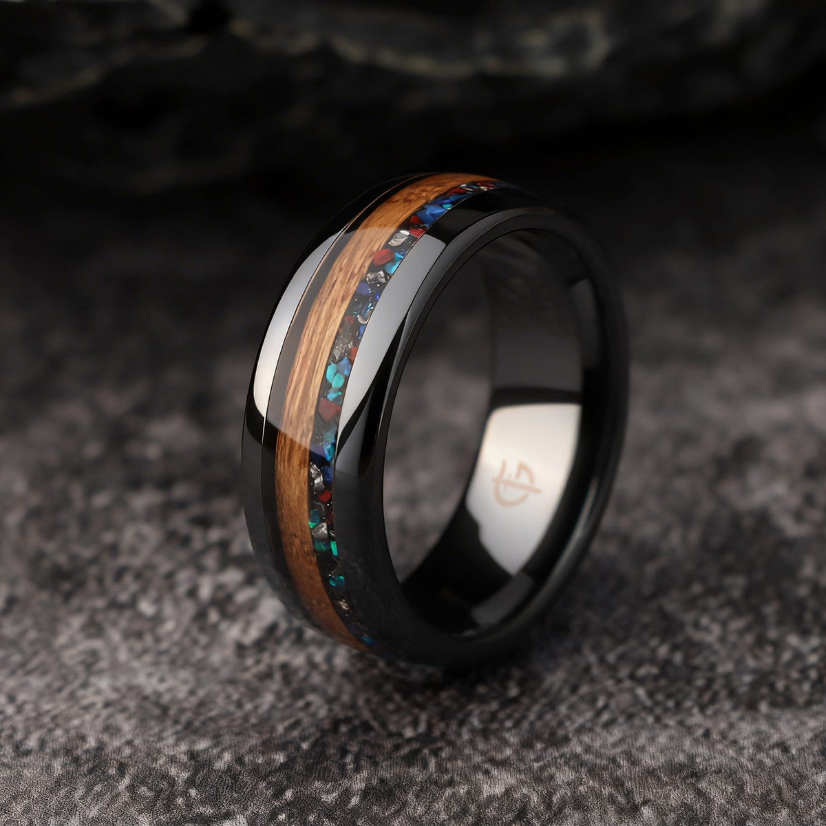 Polished black ceramic ring with brown wood beside blue-green, red and silver-gray inlay fragments.