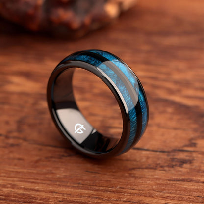 Polished black ceramic ring with two blue whiskey barrel wood inlays separated by a black center strip.