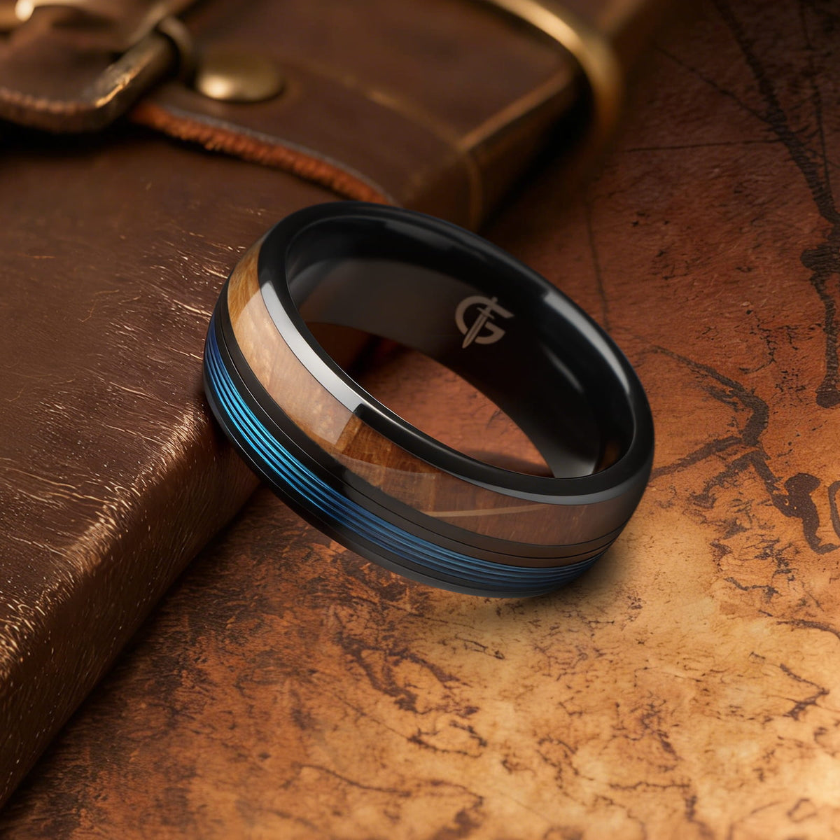 Black ceramic ring with brown whiskey barrel wood and blue fishing line inlays separated by a black strip.