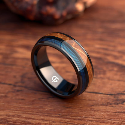 Black ceramic ring with brown whiskey barrel wood and blue fishing line inlays separated by a black strip.