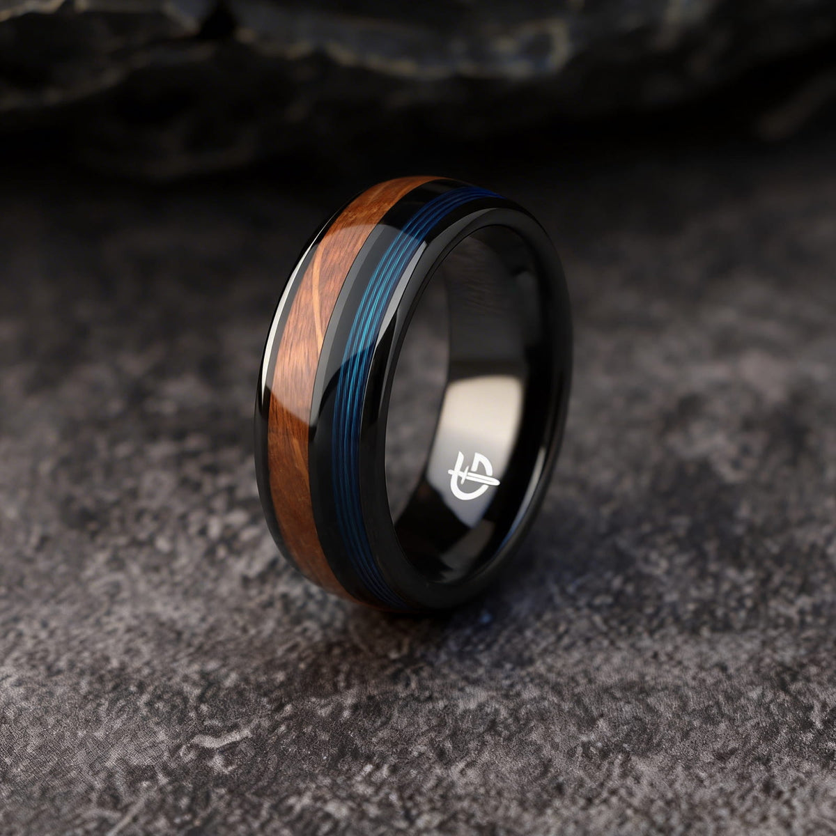 Black ceramic ring with brown whiskey barrel wood and blue fishing line inlays separated by a black strip.