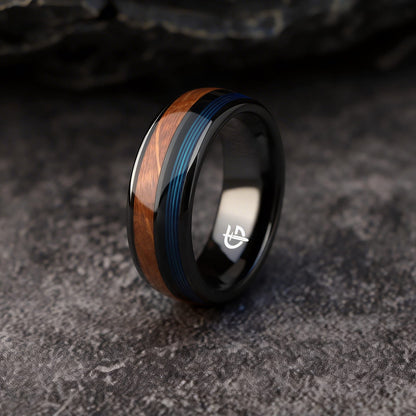 Black ceramic ring with brown whiskey barrel wood and blue fishing line inlays separated by a black strip.