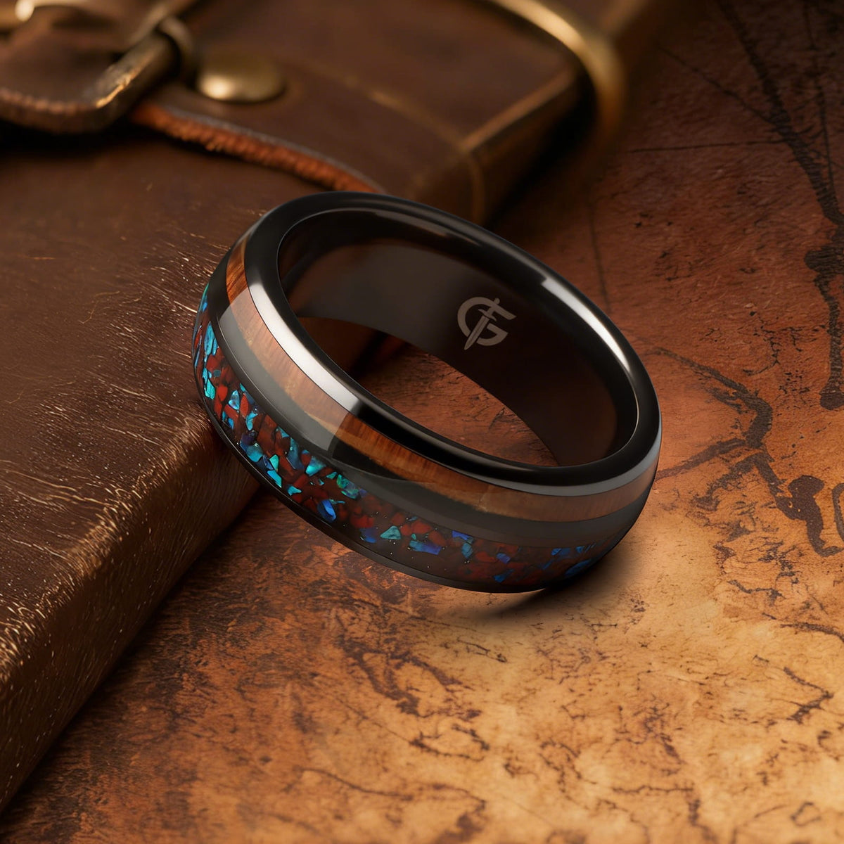 Black ceramic ring with reddish dinosaur bone and blue natural opal beside brown whiskey barrel wood