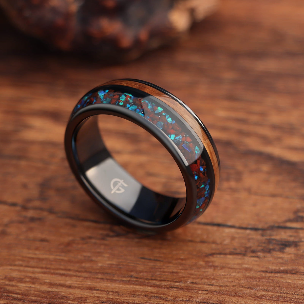 Black ceramic ring with reddish dinosaur bone and blue natural opal beside brown whiskey barrel wood