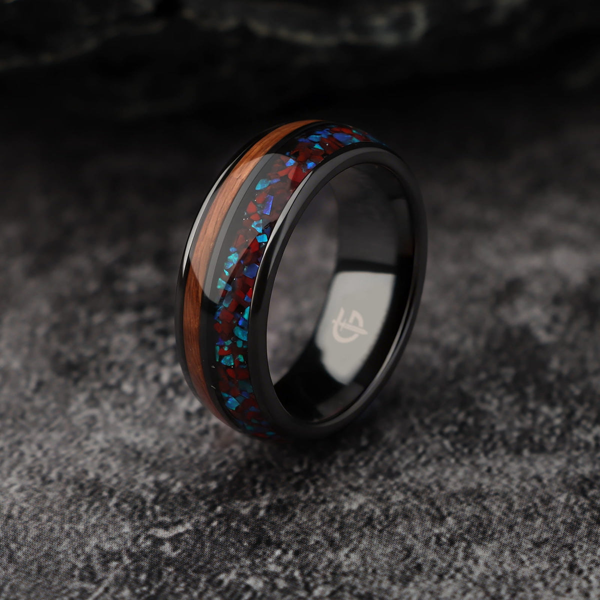 Black ceramic ring with reddish dinosaur bone and blue natural opal beside brown whiskey barrel wood
