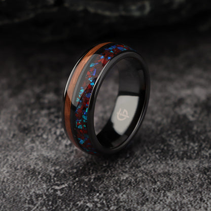 Black ceramic ring with reddish dinosaur bone and blue natural opal beside brown whiskey barrel wood