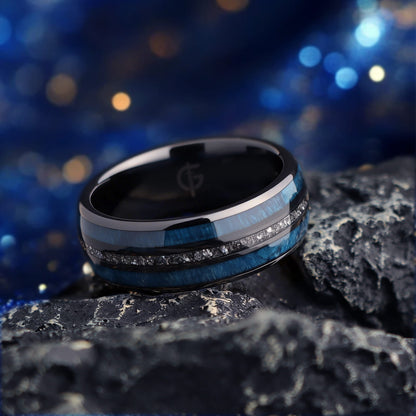 Polished black ceramic ring with two blue whiskey barrel wood bands framing silver-gray Gibeon meteorite fragments.