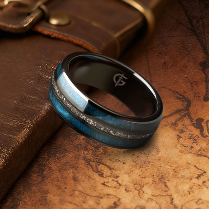 Polished black ceramic ring with two blue whiskey barrel wood bands framing silver-gray Gibeon meteorite fragments.