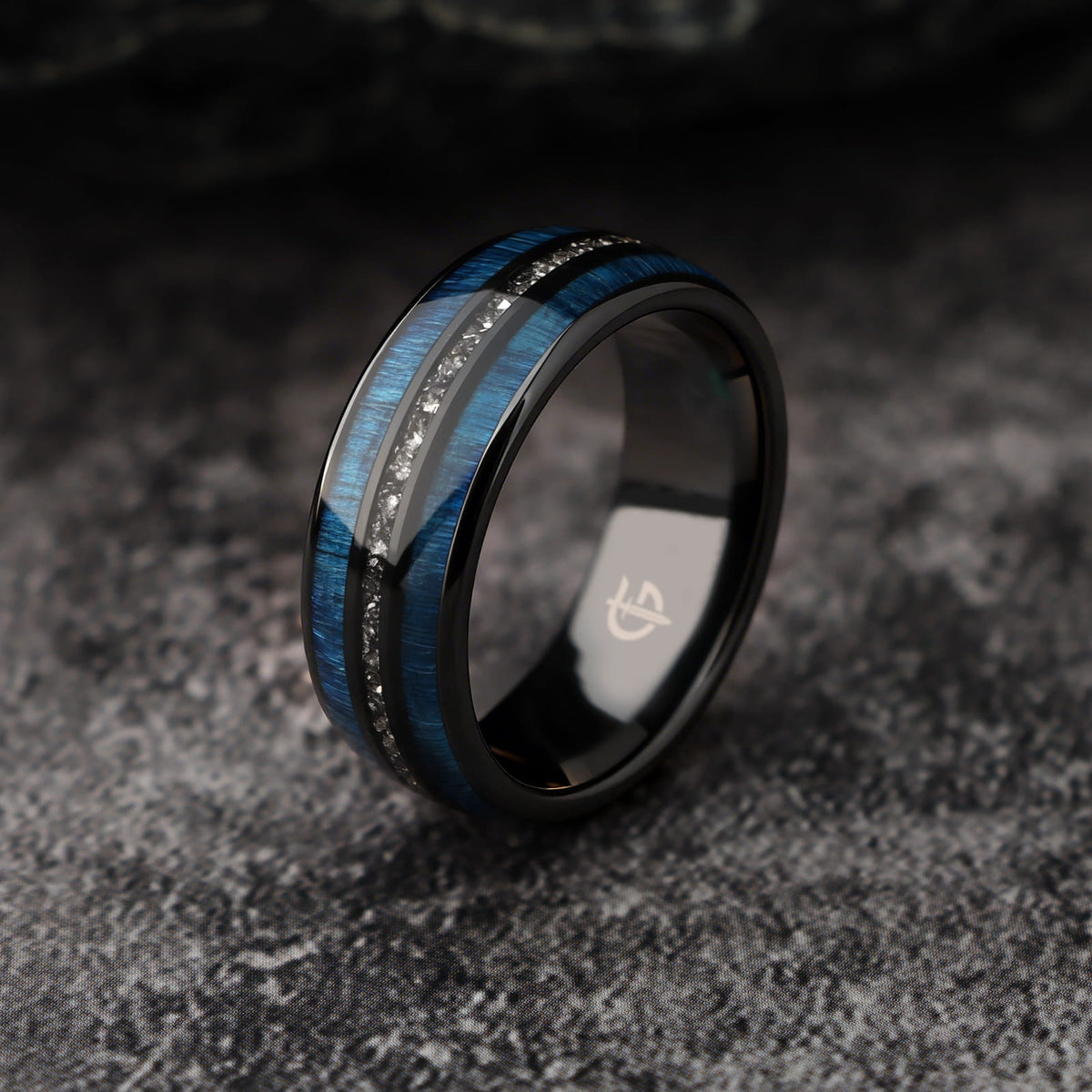 Polished black ceramic ring with two blue whiskey barrel wood bands framing silver-gray Gibeon meteorite fragments.