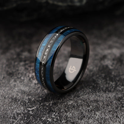 Polished black ceramic ring with two blue whiskey barrel wood bands framing silver-gray Gibeon meteorite fragments.