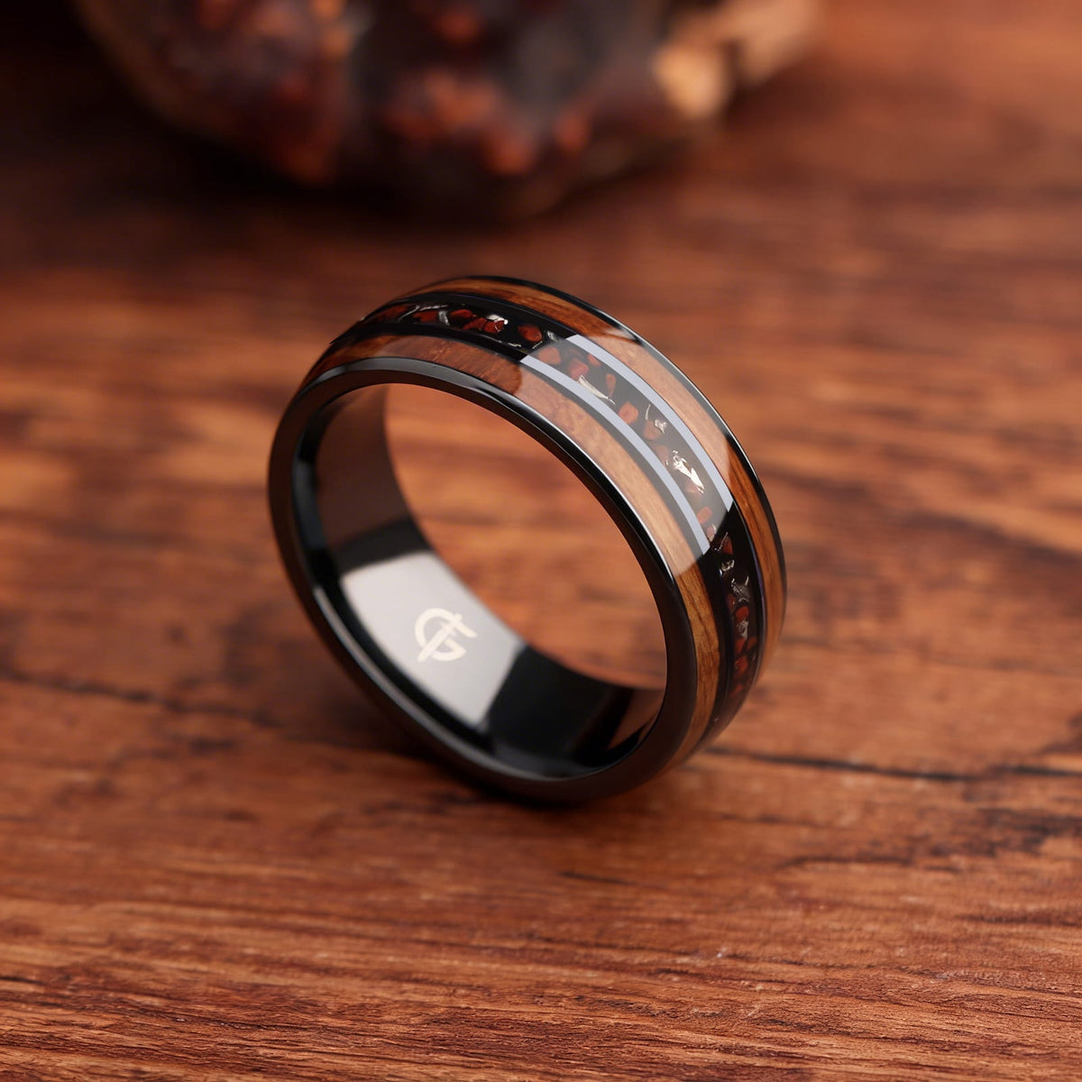 Black ceramic ring with brown wood strips framing silver-gray meteorite and reddish dinosaur bone fragments