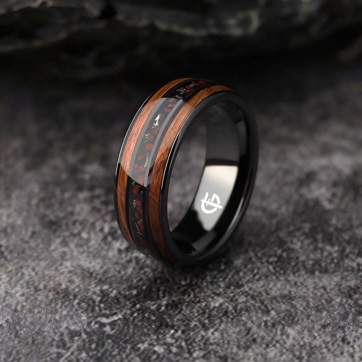 Black ceramic ring with brown wood strips framing silver-gray meteorite and reddish dinosaur bone fragments