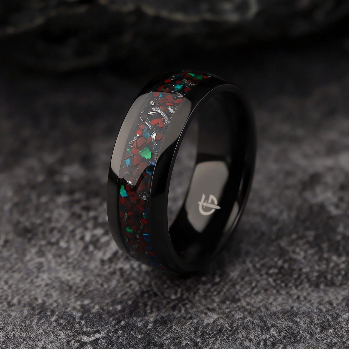 Polished black titanium ring with a mixed inlay of red, blue-green and silver-gray fragments.