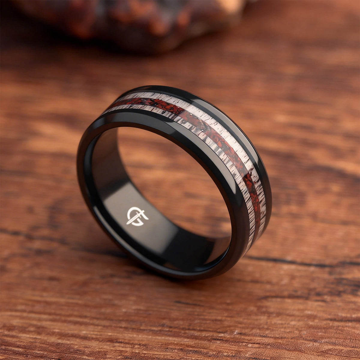 Black titanium ring with pale deer antler bands flanking a reddish mixed inlay and beveled edges