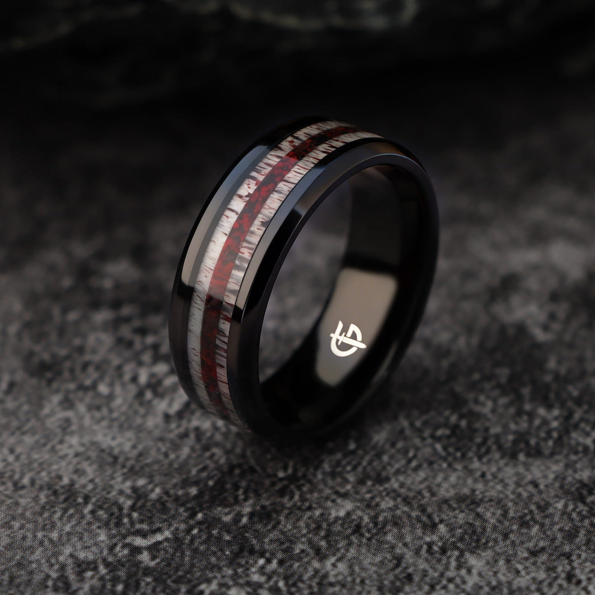 Black titanium ring with pale deer antler bands flanking a reddish mixed inlay and beveled edges