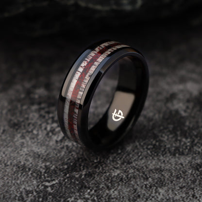 Black titanium ring with pale deer antler bands flanking a reddish mixed inlay and beveled edges