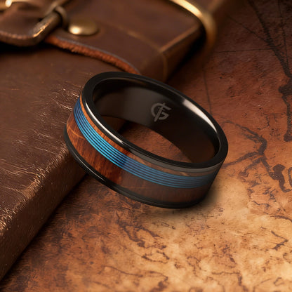 Black titanium ring with blue fishing line centered between brown whiskey barrel wood bands