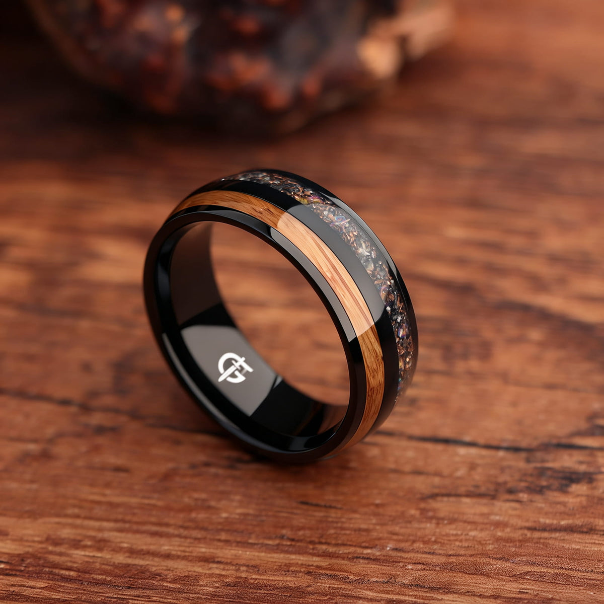 Black titanium ring with whiskey barrel wood beside a silver-gray meteorite, moonstone and copper inlay.