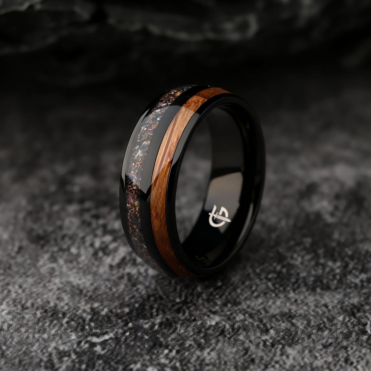 Black titanium ring with whiskey barrel wood beside a silver-gray meteorite, moonstone and copper inlay.