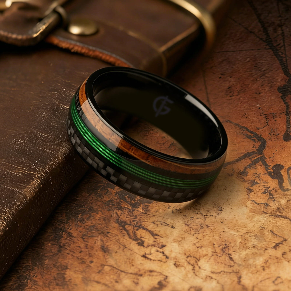 Black titanium ring with green fishing line between brown whiskey barrel wood and black carbon fiber