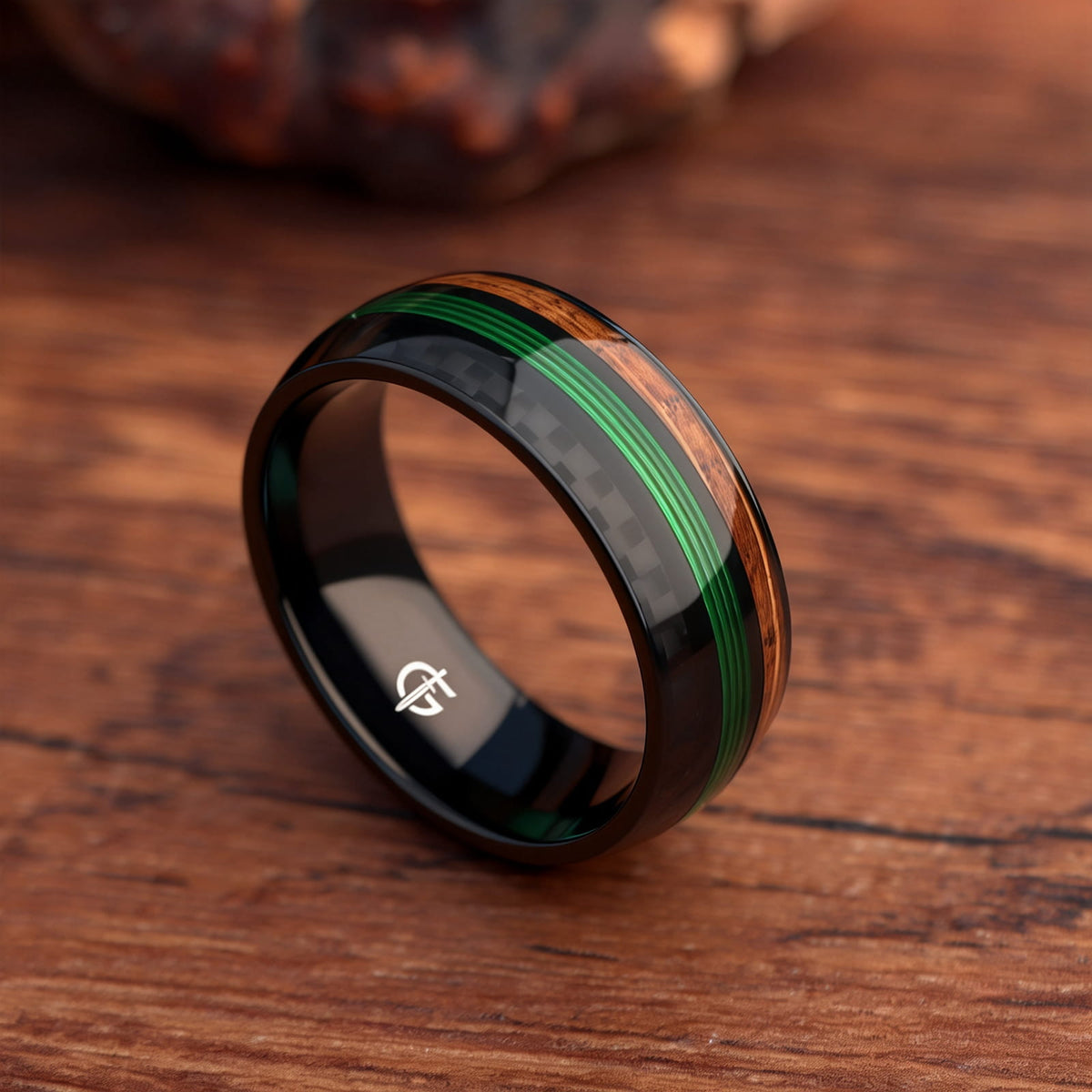 Black titanium ring with green fishing line between brown whiskey barrel wood and black carbon fiber