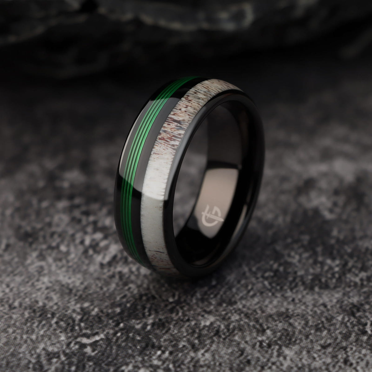 Polished black tungsten ring with pale deer antler beside parallel green fishing line strands