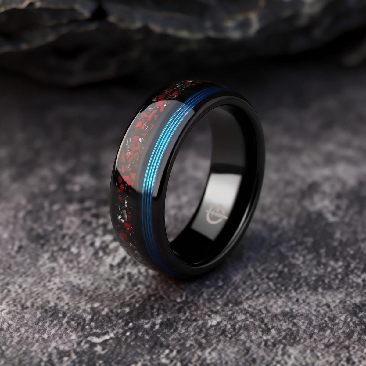 Polished black tungsten ring with fine blue fishing line beside red dinosaur bone and silver-gray meteorite fragments