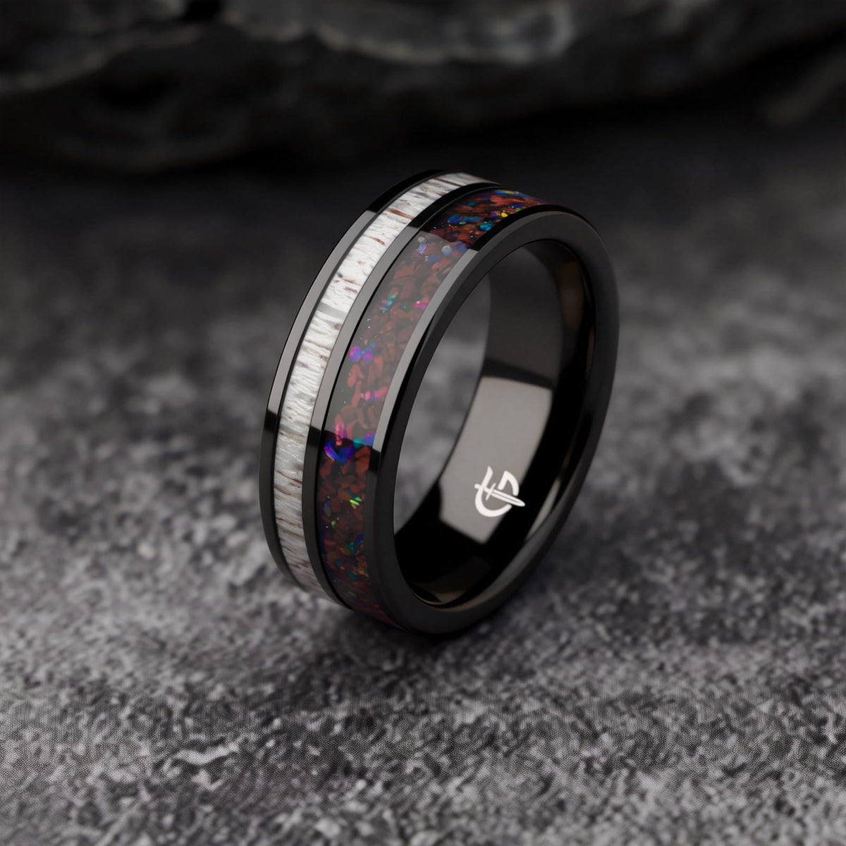 Polished black tungsten ring with pale deer antler beside red dinosaur bone and multicolored natural opal