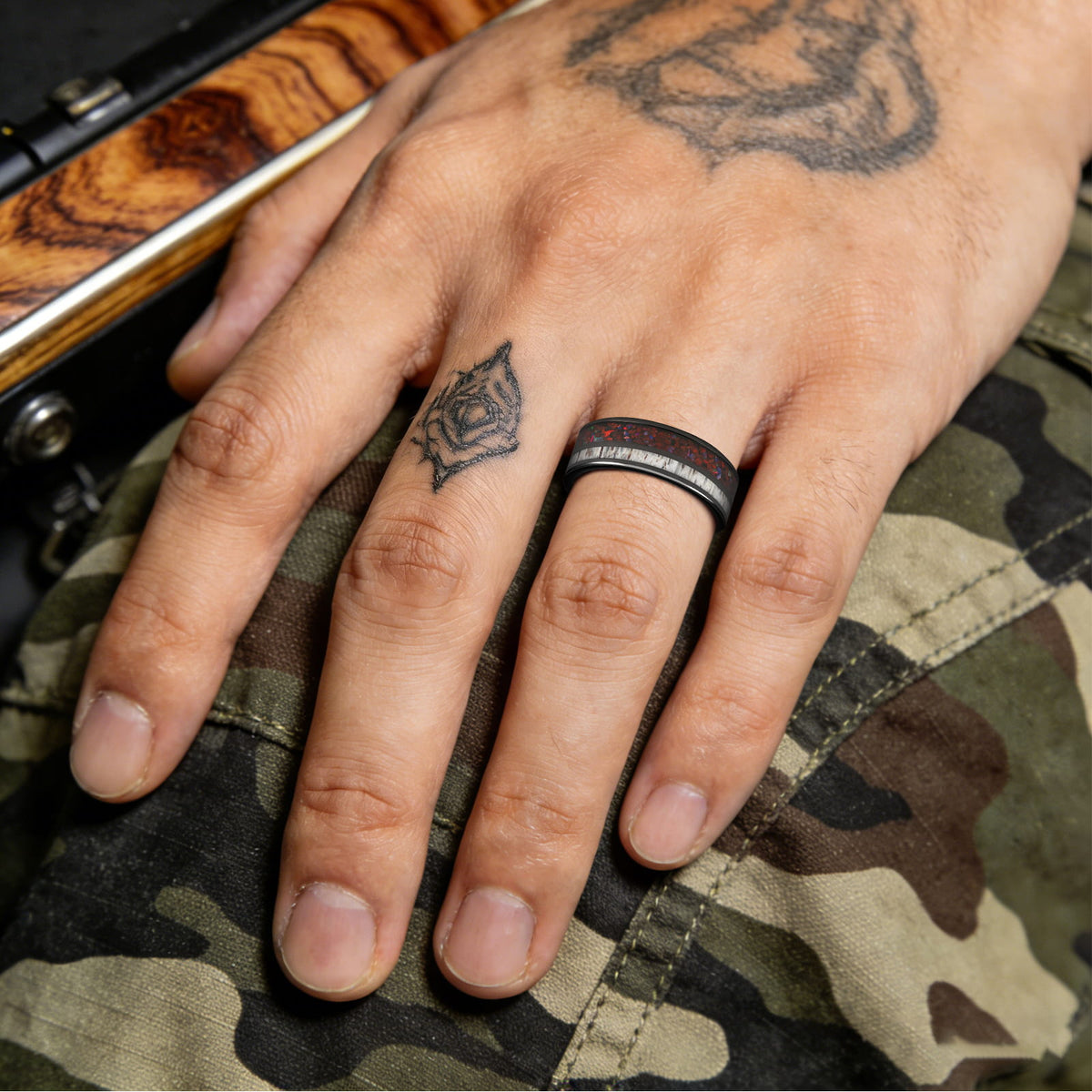 Polished black tungsten ring with pale deer antler beside red dinosaur bone and multicolored natural opal