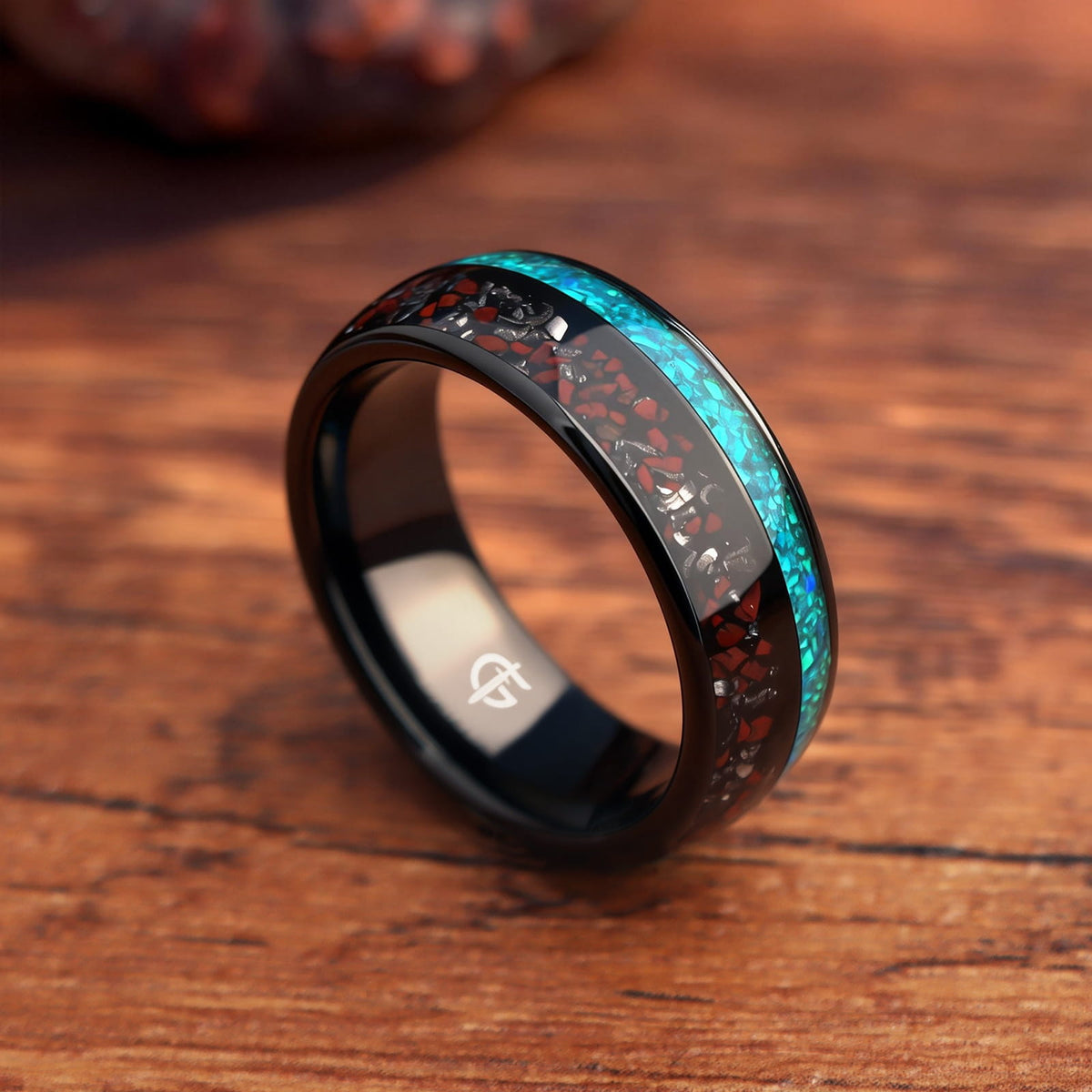 Black domed tungsten ring with red and silver-gray fragments beside a blue-green opal inlay.