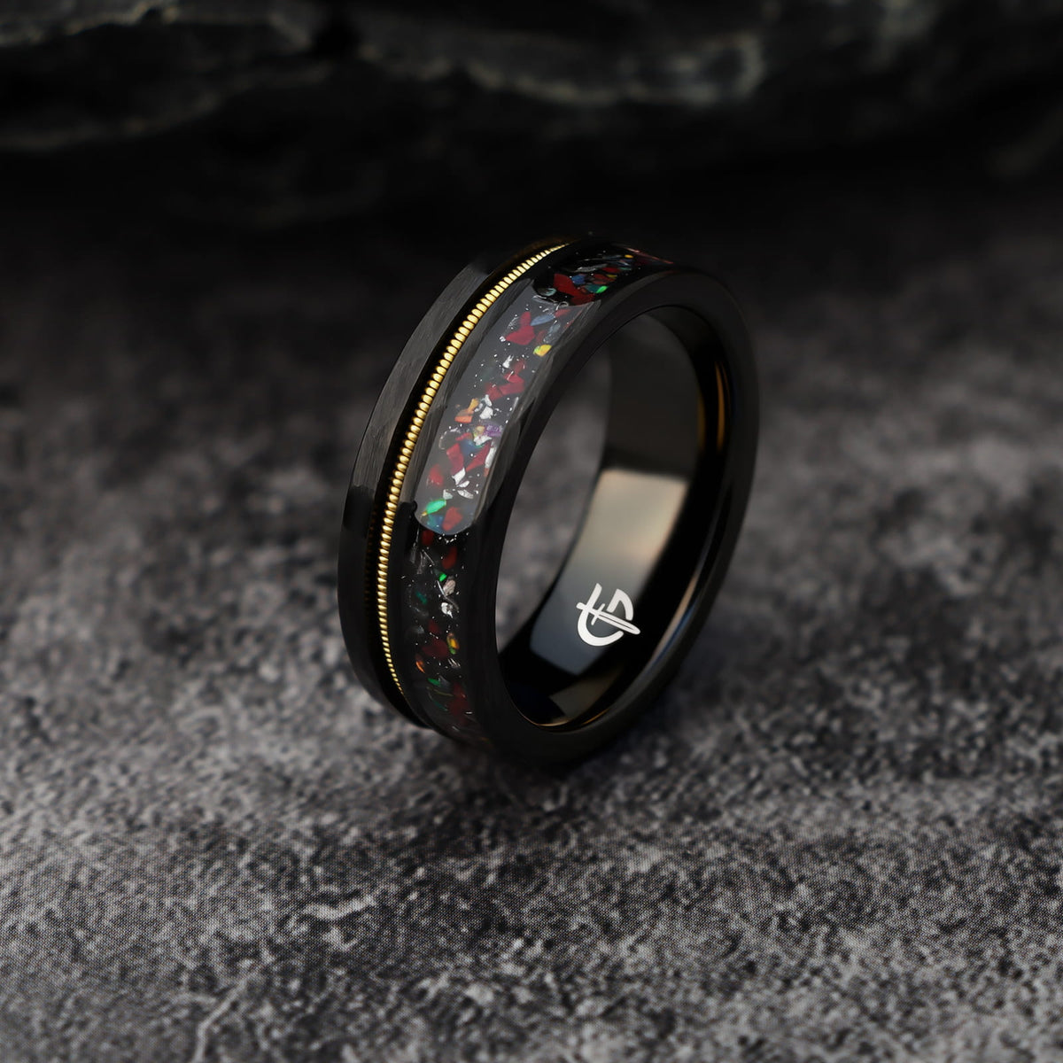 Hammered black tungsten carbide ring with a gold-tone guitar string and red-brown, silver-gray and multicolor inlays