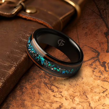 Black domed ring with two wood strips framing a center inlay of silver-gray and blue-green fragments.