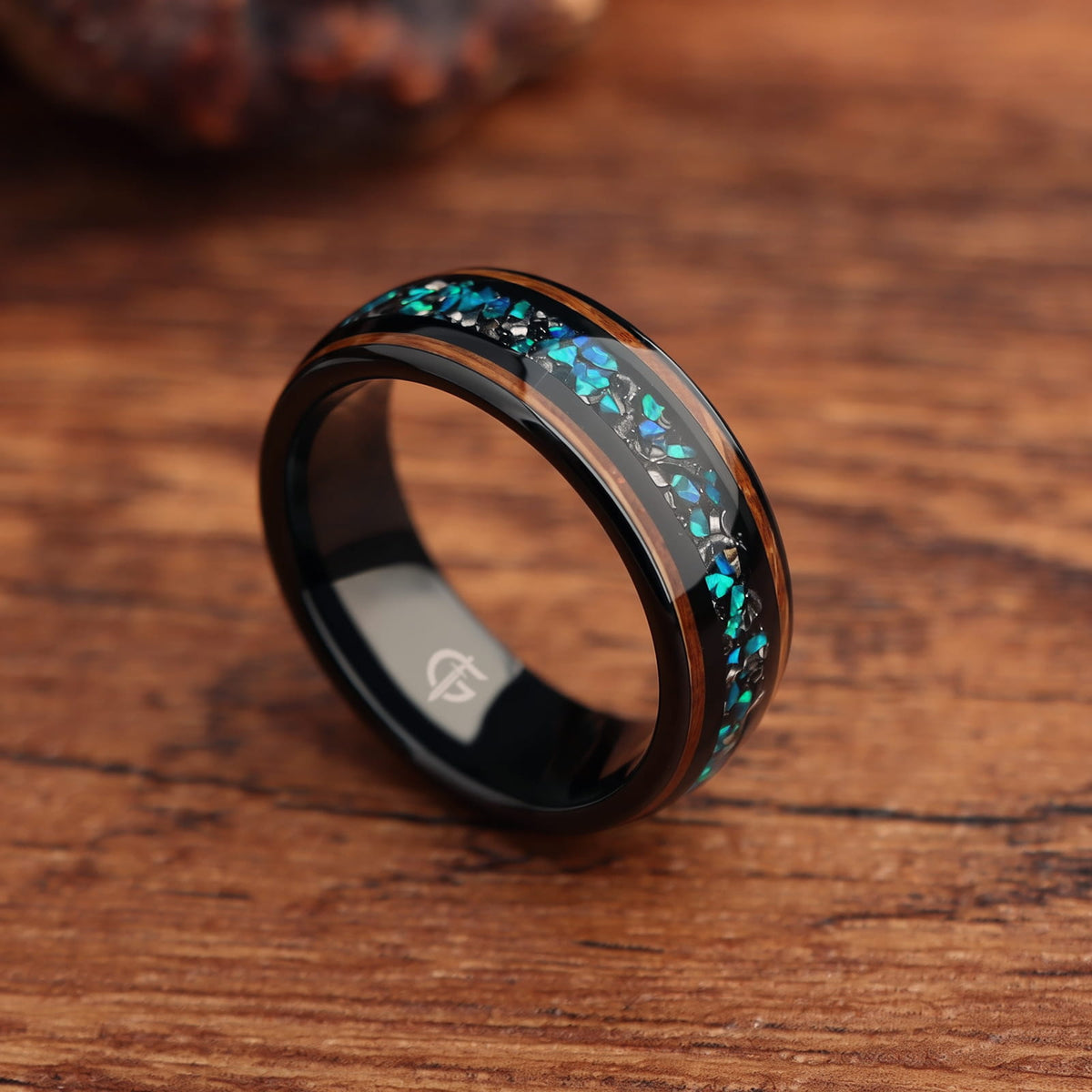 Black domed ring with two wood strips framing a center inlay of silver-gray and blue-green fragments.