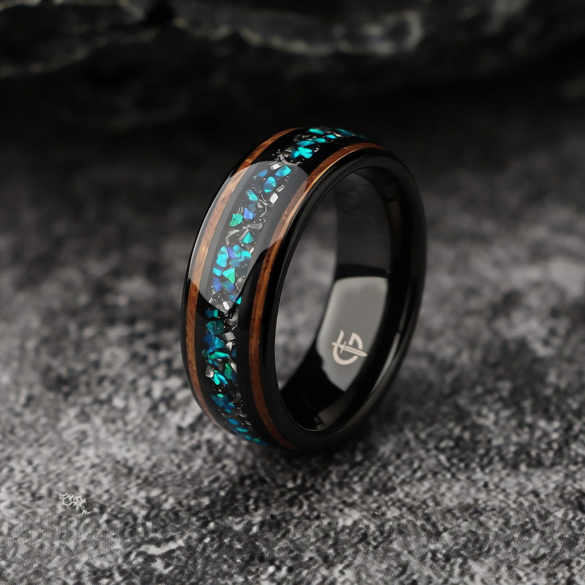 Black domed ring with two wood strips framing a center inlay of silver-gray and blue-green fragments.