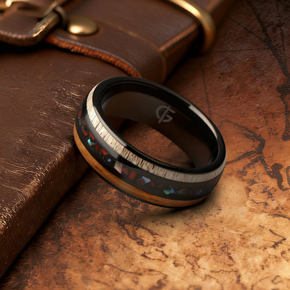 Black tungsten ring with wood and pale antler framing red dinosaur bone and iridescent abalone shell