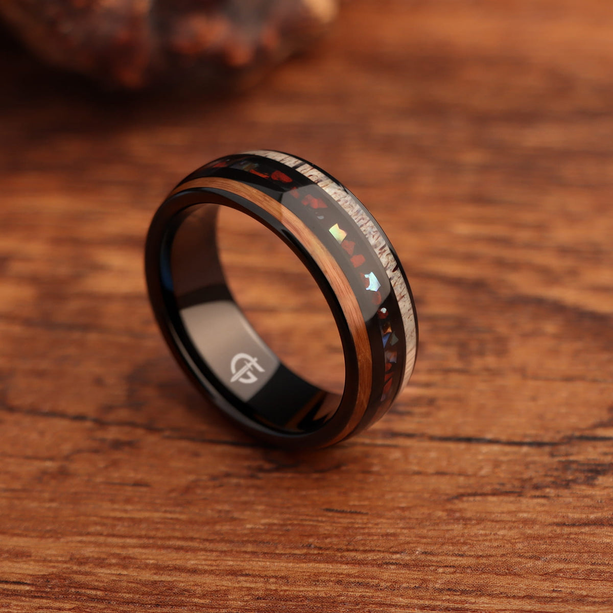 Black tungsten ring with wood and pale antler framing red dinosaur bone and iridescent abalone shell