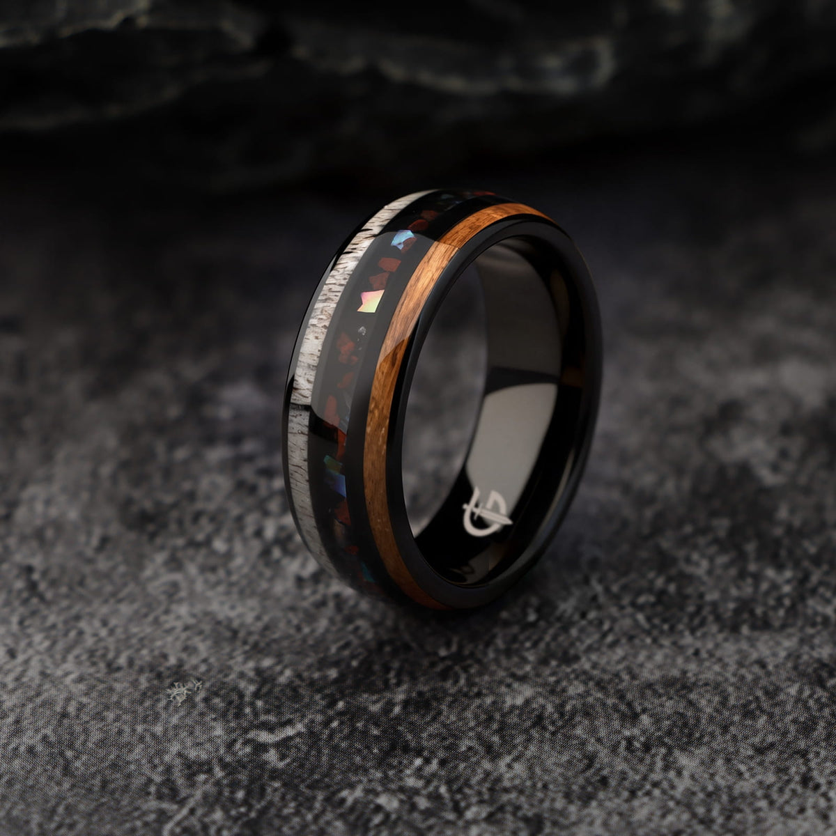 Black tungsten ring with wood and pale antler framing red dinosaur bone and iridescent abalone shell