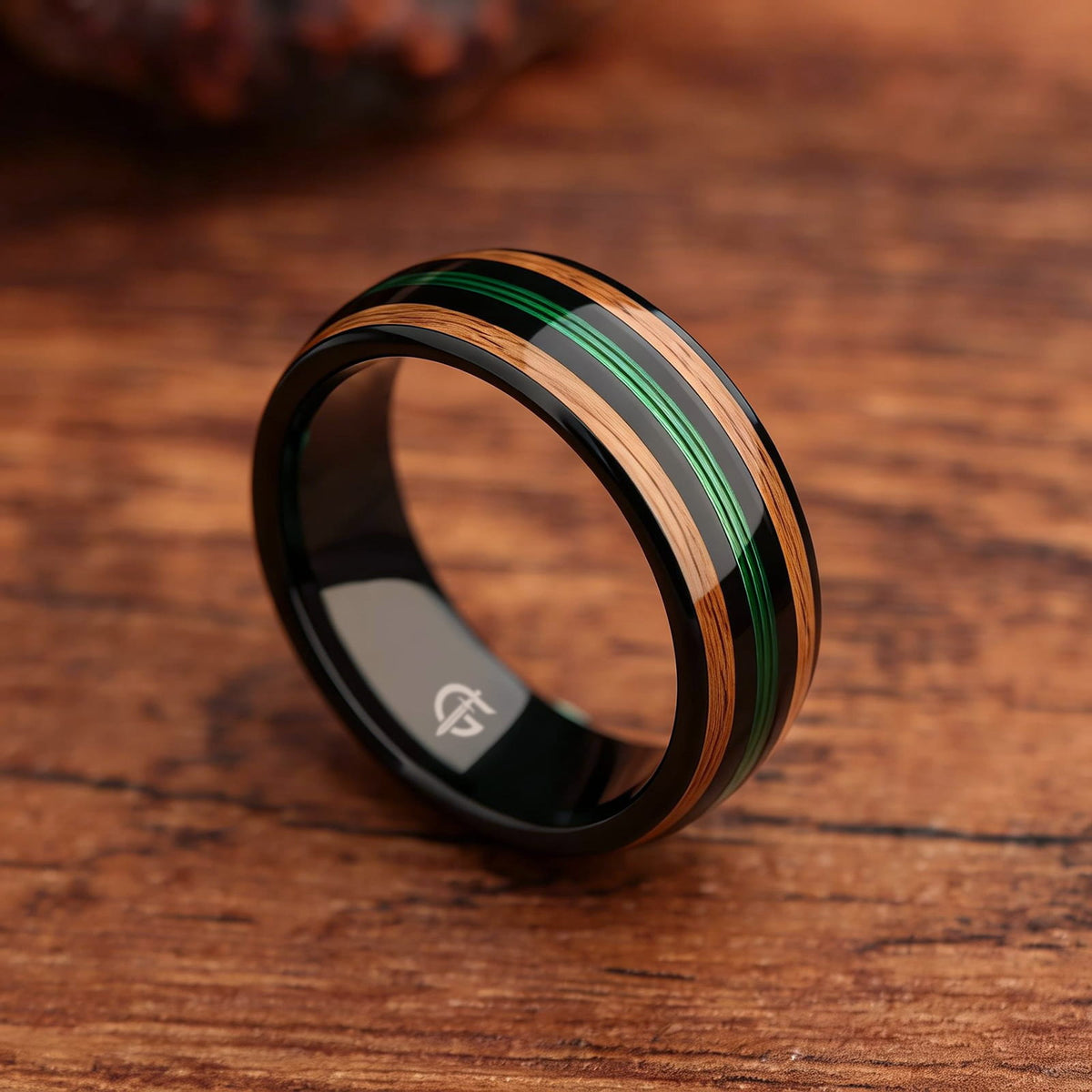 Polished black tungsten ring with green fishing line between two brown whiskey barrel wood bands