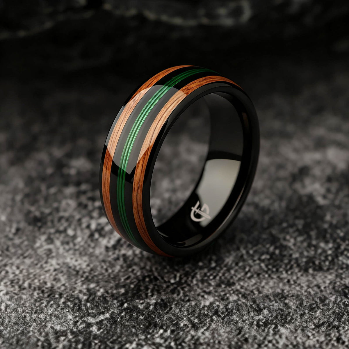 Polished black tungsten ring with green fishing line between two brown whiskey barrel wood bands